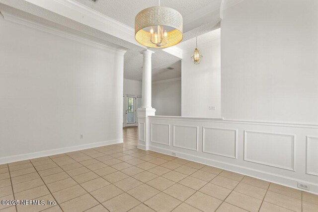 empty room with crown molding, light tile patterned floors, a decorative wall, a textured ceiling, and ornate columns