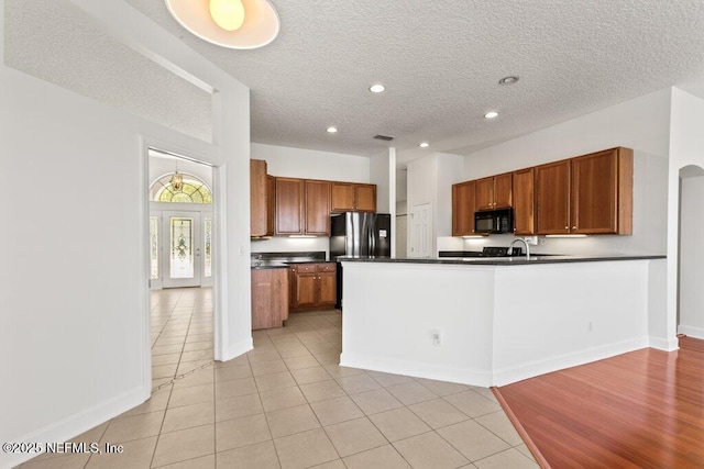 kitchen with brown cabinets, dark countertops, freestanding refrigerator, a peninsula, and black microwave