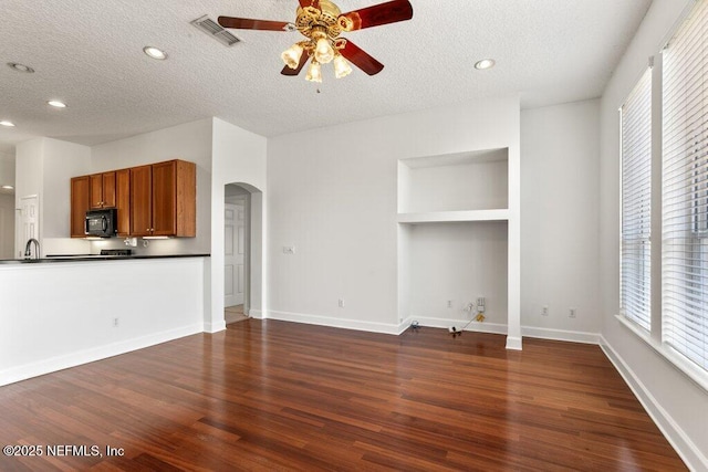 unfurnished living room featuring visible vents, dark wood-type flooring, a ceiling fan, a textured ceiling, and arched walkways
