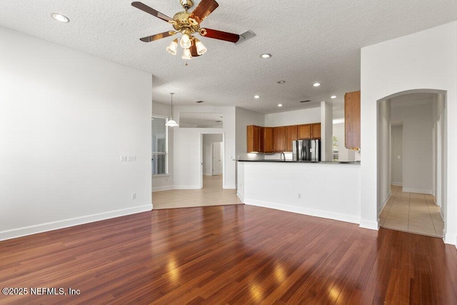 unfurnished living room with visible vents, arched walkways, a textured ceiling, a ceiling fan, and wood-type flooring