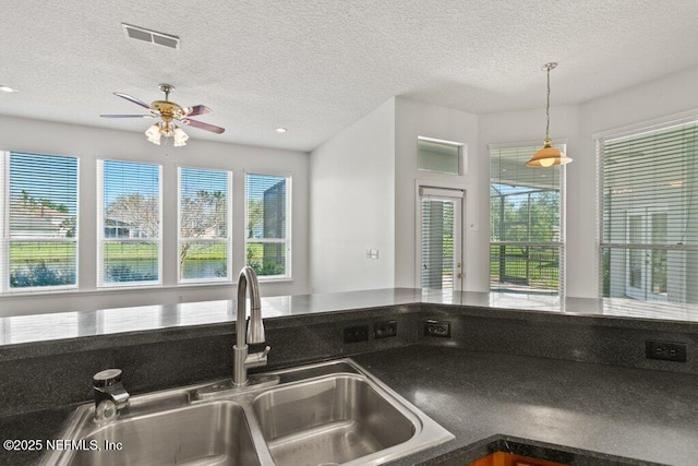 kitchen featuring dark countertops, a ceiling fan, visible vents, and a sink