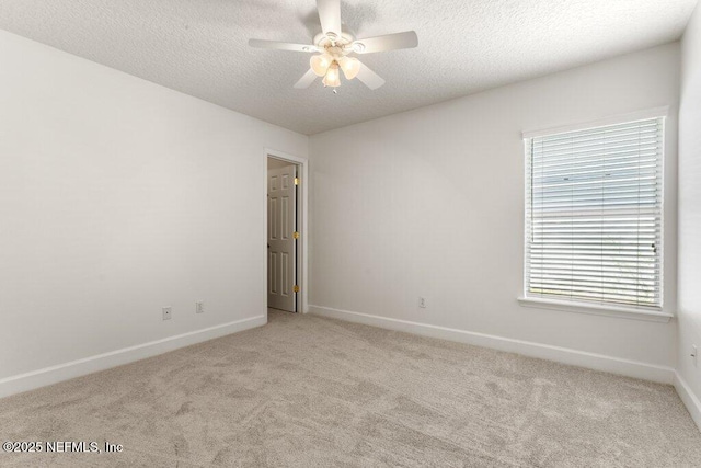 unfurnished room with a ceiling fan, light colored carpet, baseboards, and a textured ceiling