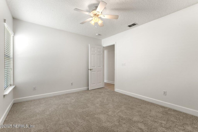empty room featuring visible vents, light carpet, a textured ceiling, baseboards, and ceiling fan