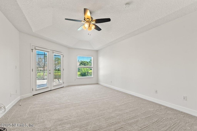 carpeted empty room featuring a tray ceiling, a ceiling fan, and baseboards
