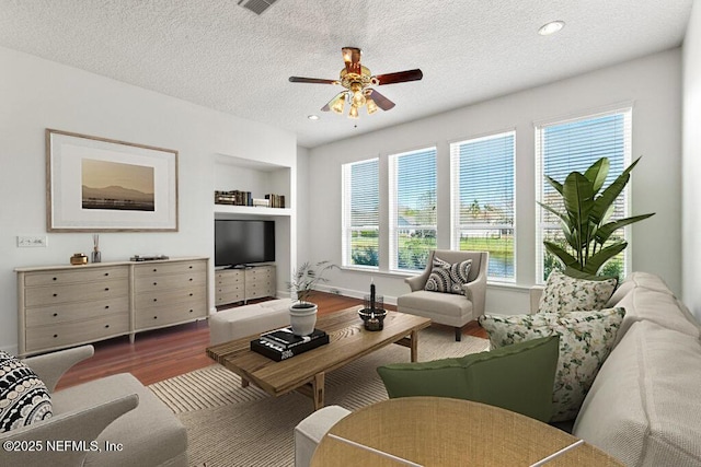 living area with a ceiling fan, built in features, a textured ceiling, wood finished floors, and recessed lighting