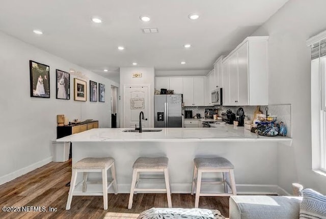 kitchen featuring sink, stainless steel appliances, hardwood / wood-style floors, a kitchen bar, and white cabinets