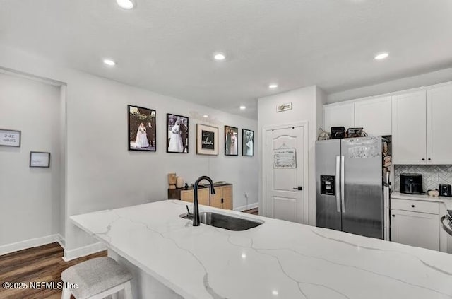 kitchen featuring white cabinetry, sink, light stone counters, stainless steel refrigerator with ice dispenser, and decorative backsplash