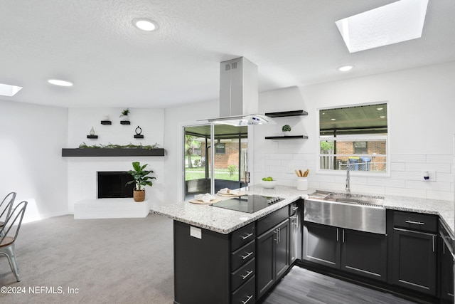 kitchen featuring island exhaust hood, kitchen peninsula, light stone countertops, a wealth of natural light, and black electric cooktop