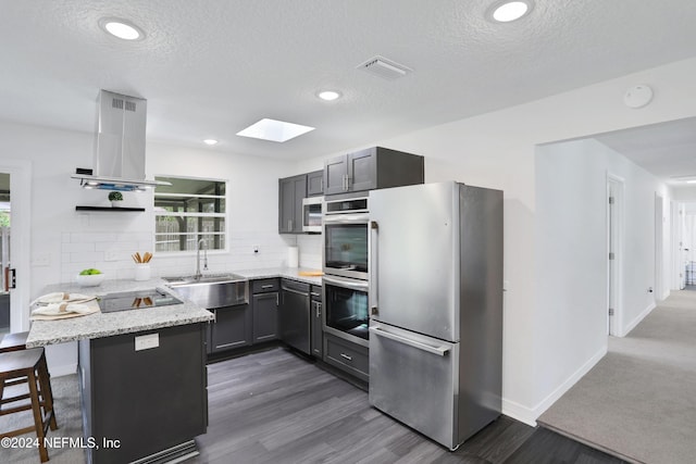 kitchen featuring backsplash, a breakfast bar area, kitchen peninsula, island exhaust hood, and stainless steel appliances