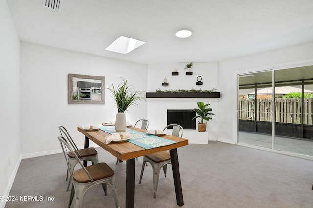 carpeted dining space with a skylight and a brick fireplace