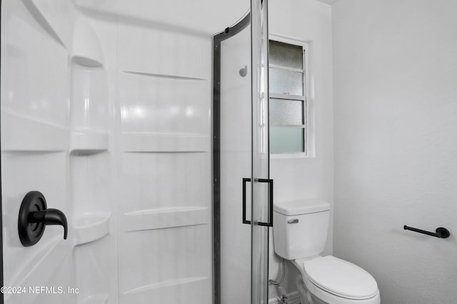 bathroom featuring a shower with shower door and toilet