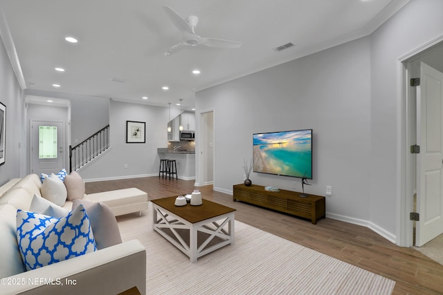 living room with light hardwood / wood-style floors, ceiling fan, and ornamental molding