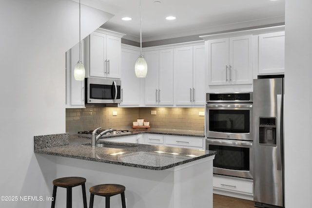 kitchen featuring kitchen peninsula, stainless steel appliances, dark stone countertops, white cabinets, and hanging light fixtures