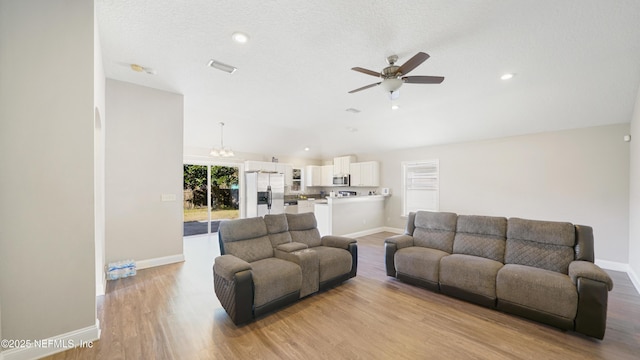 living room featuring a textured ceiling, ceiling fan with notable chandelier, and light hardwood / wood-style floors