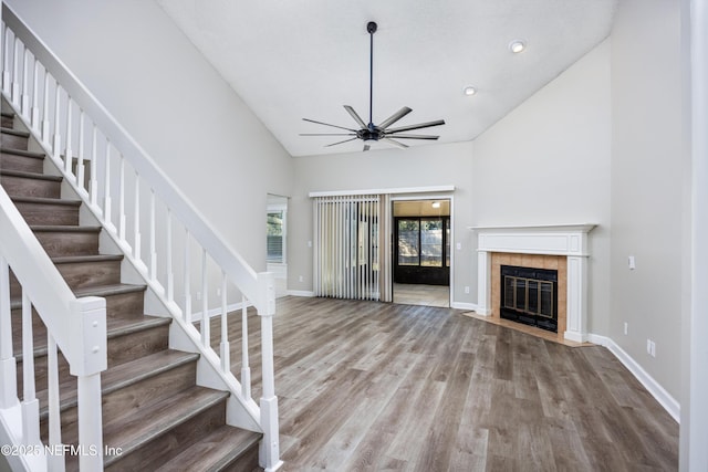 unfurnished living room featuring a tiled fireplace, hardwood / wood-style floors, high vaulted ceiling, and ceiling fan