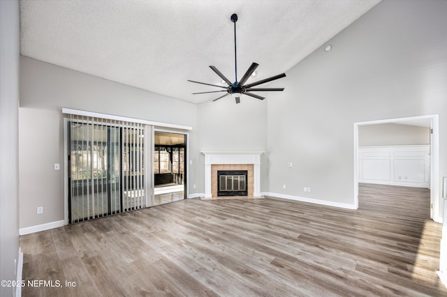 unfurnished living room with a tiled fireplace, ceiling fan, a textured ceiling, and light wood-type flooring