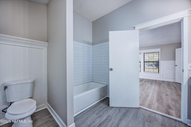 bathroom featuring toilet, hardwood / wood-style floors, a textured ceiling, and a tub