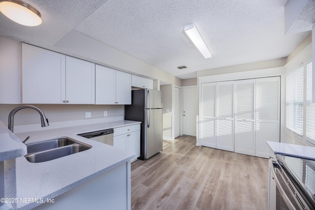 kitchen with sink, appliances with stainless steel finishes, white cabinetry, a textured ceiling, and light wood-type flooring