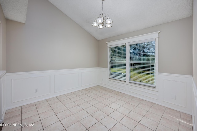 tiled empty room featuring vaulted ceiling, a notable chandelier, and a textured ceiling