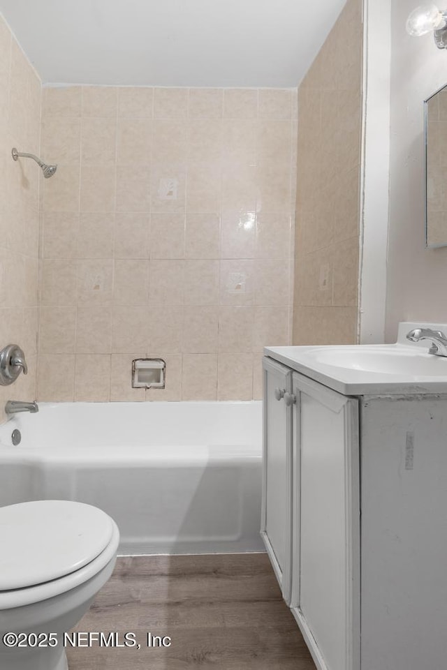 full bathroom with hardwood / wood-style floors, vanity, tiled shower / bath combo, and toilet