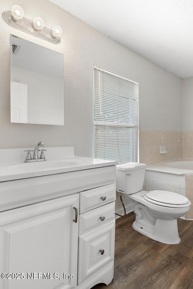 bathroom featuring vanity, toilet, wood-type flooring, and tiled tub