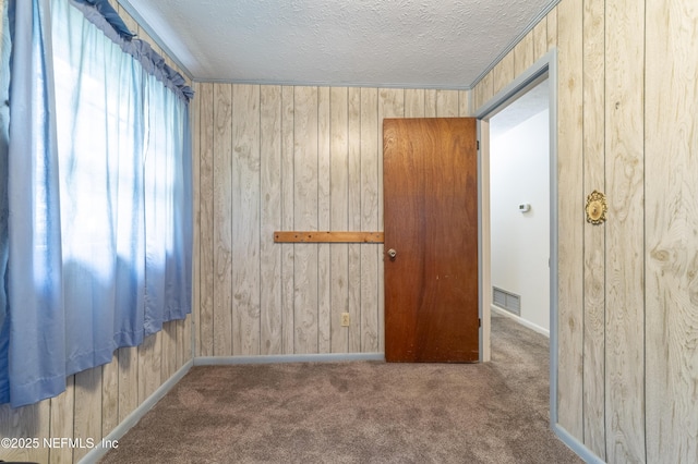 carpeted spare room with wood walls and a textured ceiling