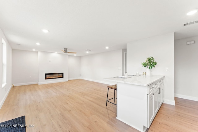 kitchen with white cabinets, a kitchen breakfast bar, ceiling fan, and light hardwood / wood-style flooring