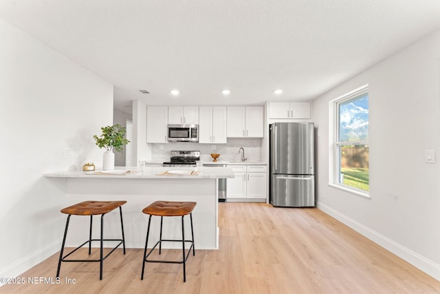 kitchen with a breakfast bar, backsplash, appliances with stainless steel finishes, light stone counters, and white cabinetry