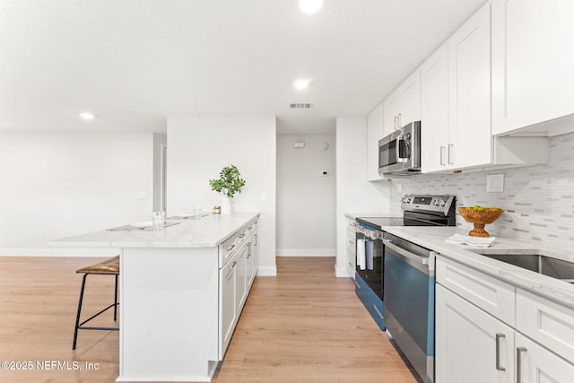 kitchen with white cabinets, appliances with stainless steel finishes, a kitchen island with sink, and a kitchen breakfast bar