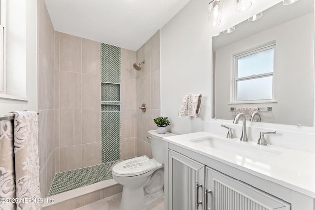 bathroom featuring a tile shower, vanity, a textured ceiling, and toilet