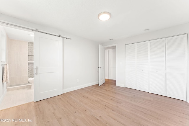 unfurnished bedroom with a barn door, light hardwood / wood-style floors, connected bathroom, and a closet