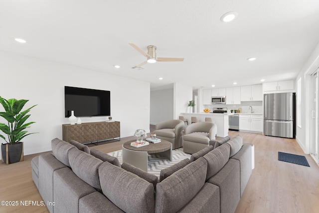 living room with light wood-type flooring, ceiling fan, and sink