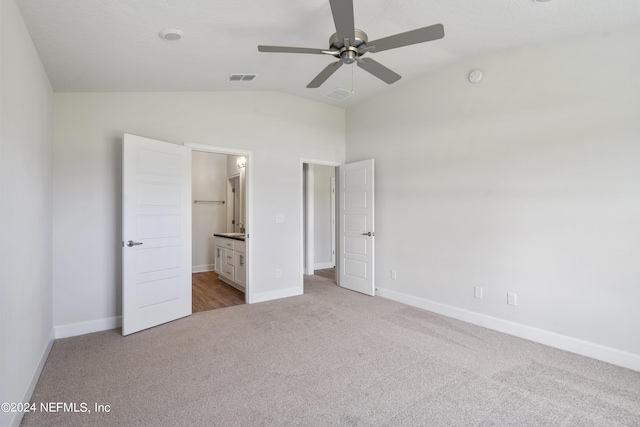 unfurnished bedroom featuring ceiling fan, light colored carpet, lofted ceiling, and connected bathroom