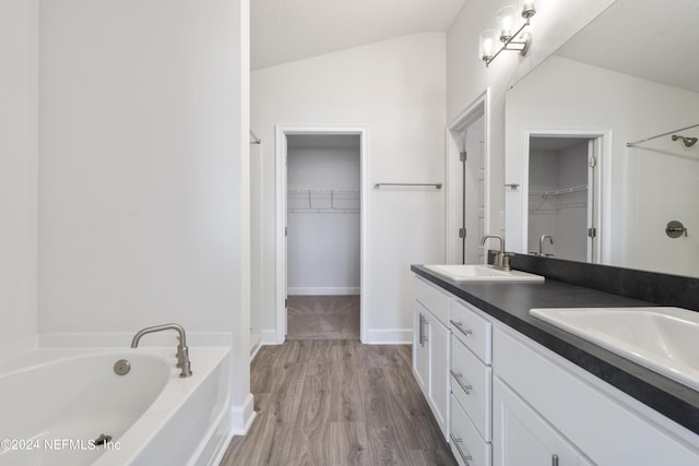 bathroom with vanity, a bath, wood-type flooring, and vaulted ceiling