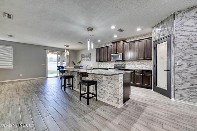 kitchen featuring a kitchen bar, appliances with stainless steel finishes, dark brown cabinetry, a kitchen island with sink, and pendant lighting