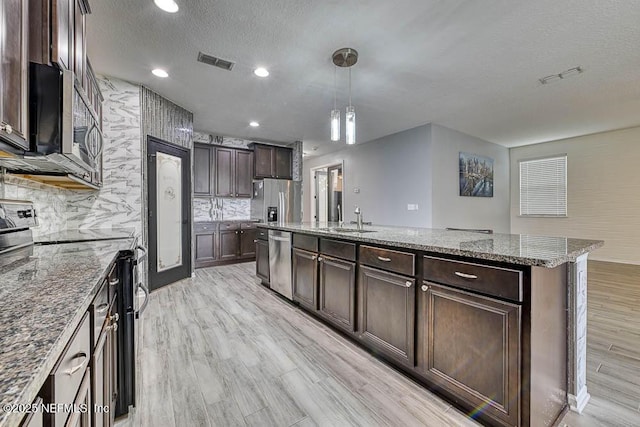 kitchen with pendant lighting, a center island with sink, stainless steel appliances, and a textured ceiling