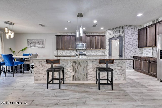 kitchen with a breakfast bar, stainless steel appliances, decorative light fixtures, and a kitchen island with sink