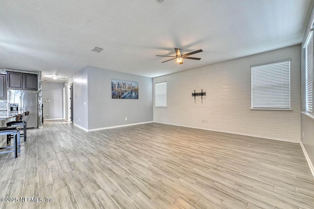 unfurnished living room with ceiling fan, light hardwood / wood-style floors, and a textured ceiling