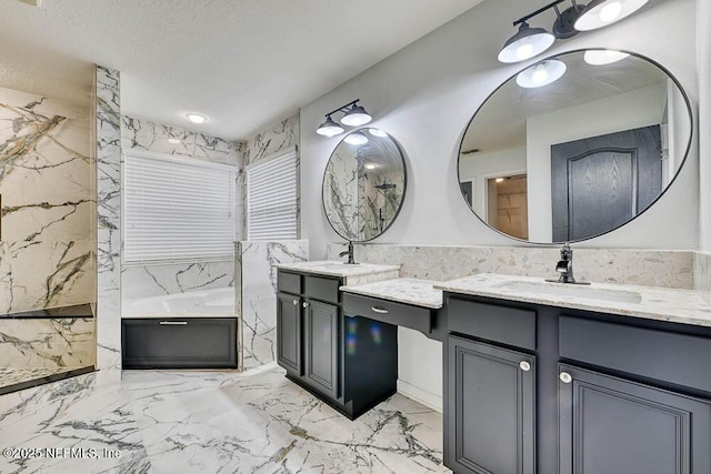 bathroom with a textured ceiling, vanity, and a tub to relax in