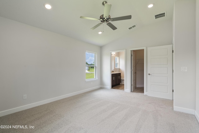 unfurnished bedroom featuring vaulted ceiling, connected bathroom, a spacious closet, light carpet, and a closet