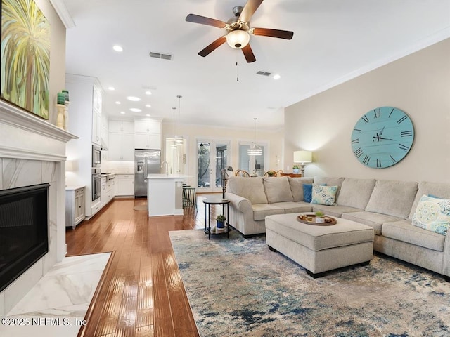 living room with ceiling fan, a fireplace, light hardwood / wood-style floors, and ornamental molding