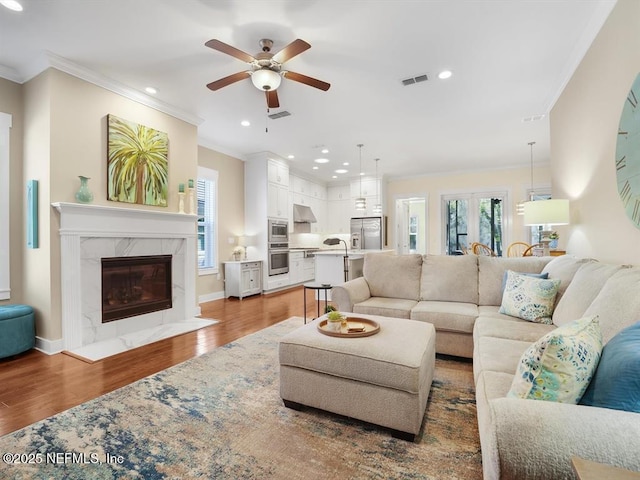 living room featuring ceiling fan, a premium fireplace, dark wood-type flooring, and ornamental molding