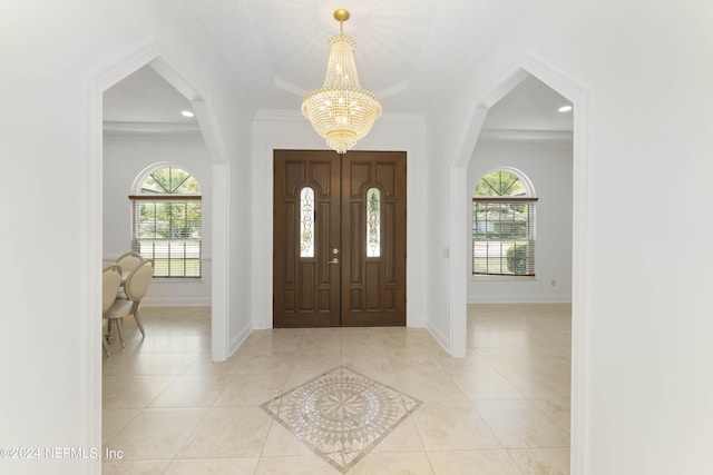 tiled foyer entrance with a healthy amount of sunlight, crown molding, and a chandelier