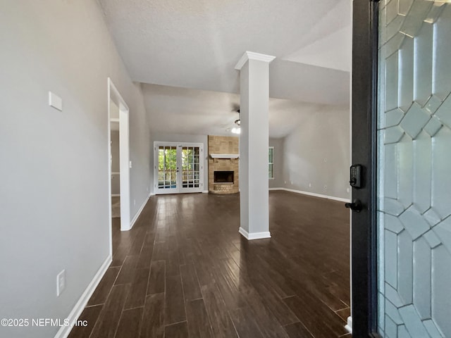 foyer entrance featuring a stone fireplace, ceiling fan, dark wood-type flooring, and vaulted ceiling