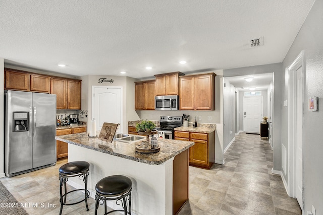 kitchen featuring a center island with sink, appliances with stainless steel finishes, a textured ceiling, a breakfast bar, and sink