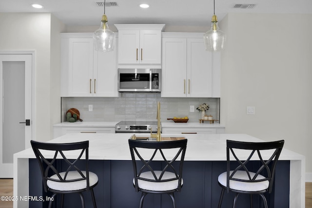 kitchen featuring backsplash, an island with sink, white cabinets, and stainless steel appliances