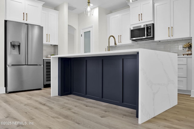 kitchen featuring white cabinets, light wood-type flooring, tasteful backsplash, stainless steel appliances, and beverage cooler