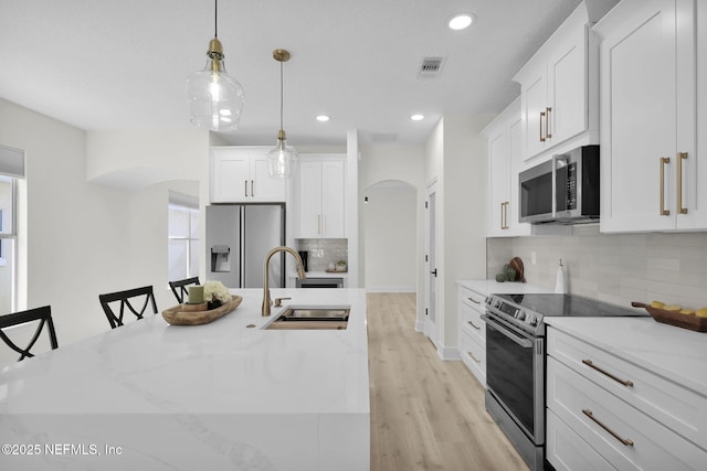 kitchen featuring pendant lighting, sink, stainless steel appliances, and an island with sink