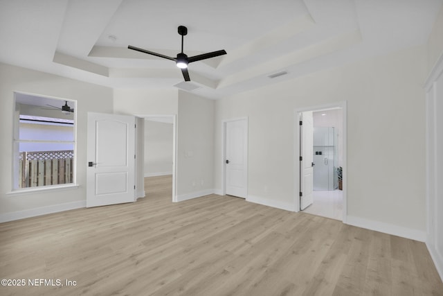 unfurnished bedroom with a raised ceiling, ceiling fan, ensuite bathroom, and light hardwood / wood-style floors