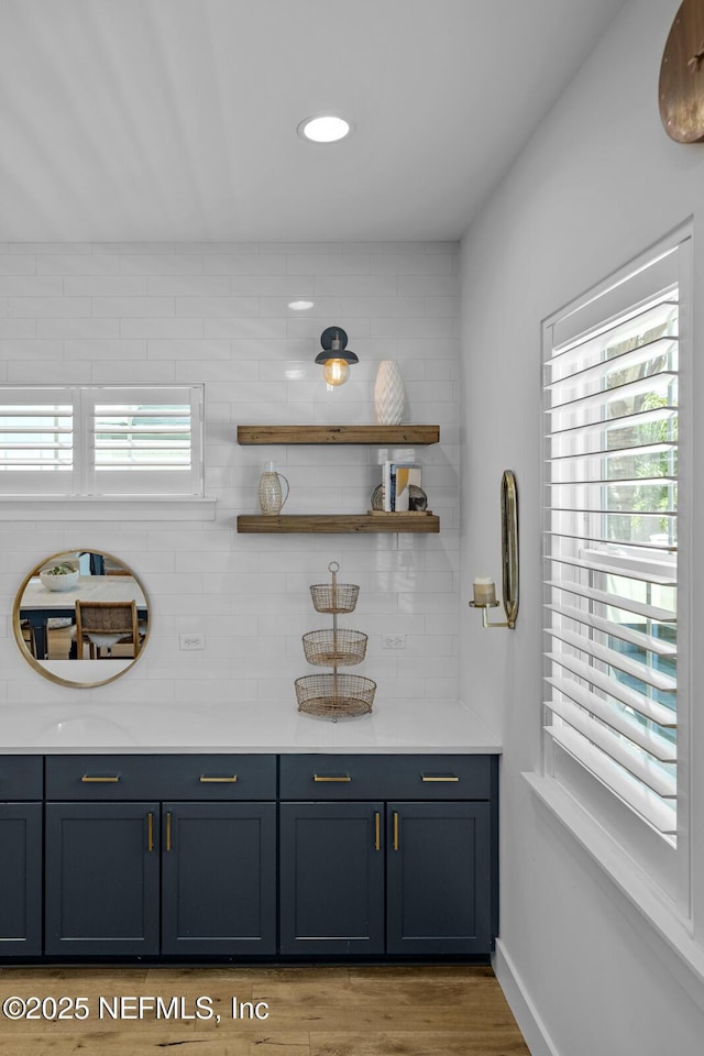 bar with decorative backsplash, light hardwood / wood-style floors, and blue cabinets